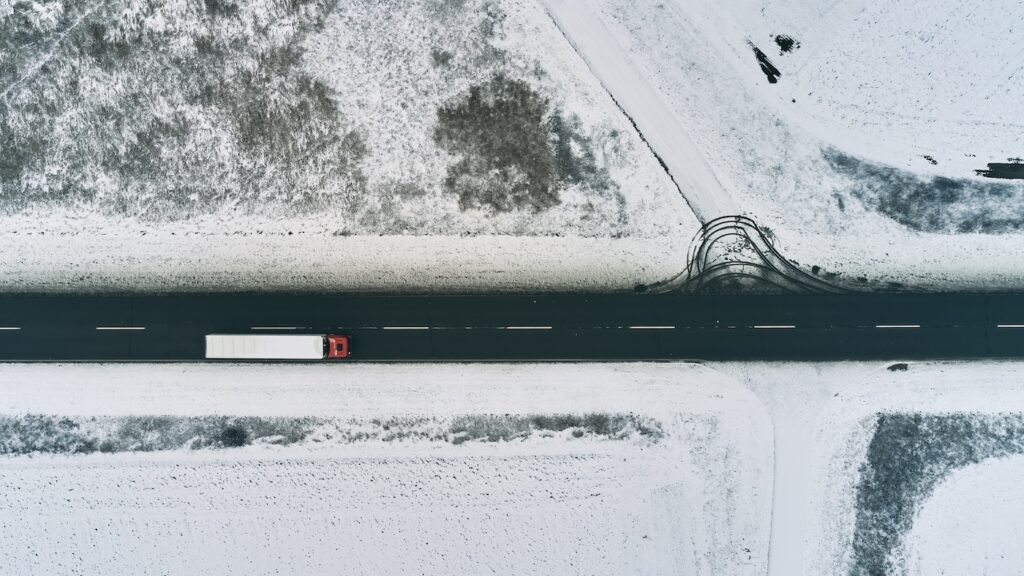 Aerial view of semi-trailer truck driving down the road in winter through countryside, top view drone pov