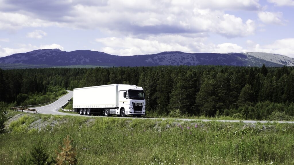 Big truck moving on a summer road. Scene. Cargo transportation in summer landscapes near a green forest and big mountains. High quality FullHD footage