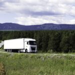 Big truck moving on a summer road. Scene. Cargo transportation in summer landscapes near a green forest and big mountains. High quality FullHD footage