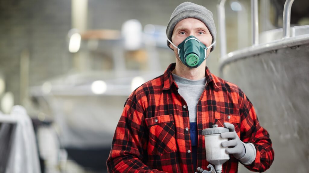 Young engineer in workwear, gloves and protective mask working with toxic and dangerous mixture