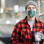 Young engineer in workwear, gloves and protective mask working with toxic and dangerous mixture