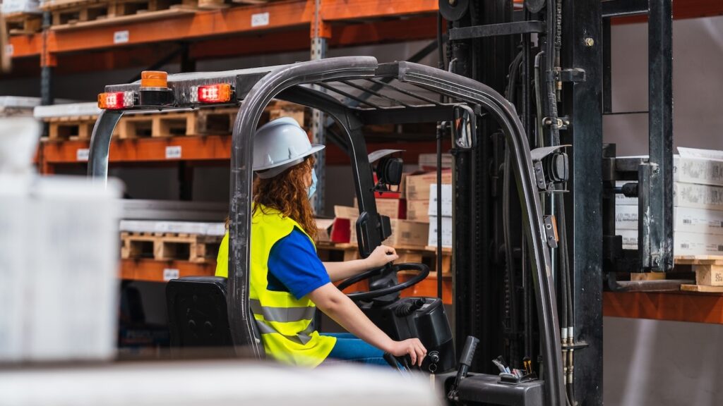 An industrial female worker using a loader in a warehouse
