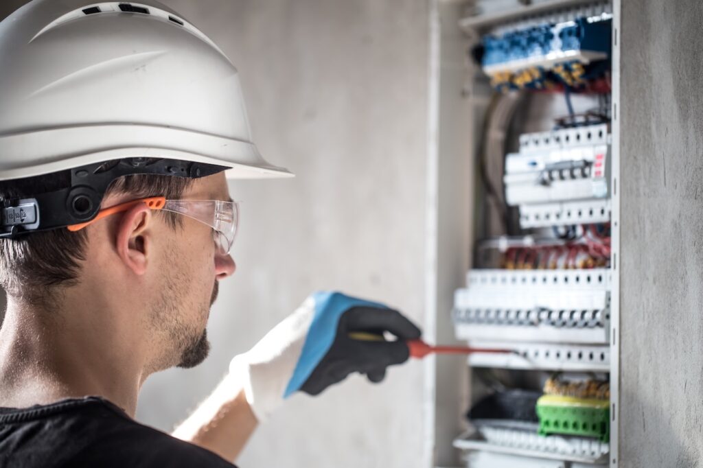 Man, an electrical technician working in a switchboard with fuses. Installation and connection of electrical equipment. Professional with tools in hand. concept of complex work, space for text.