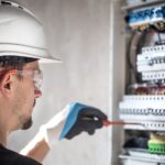 Man, an electrical technician working in a switchboard with fuses. Installation and connection of electrical equipment. Professional with tools in hand. concept of complex work, space for text.